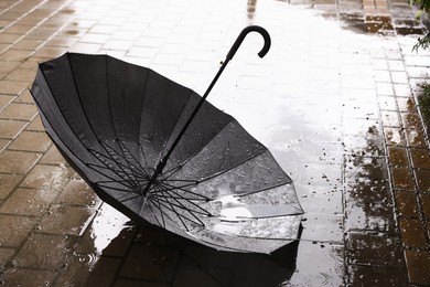 Photo of Black umbrella on wet asphalt under heavy rain, closeup. Space for text
