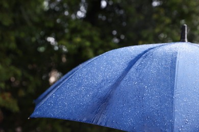 Photo of Blue umbrella under heavy rain outdoors, closeup