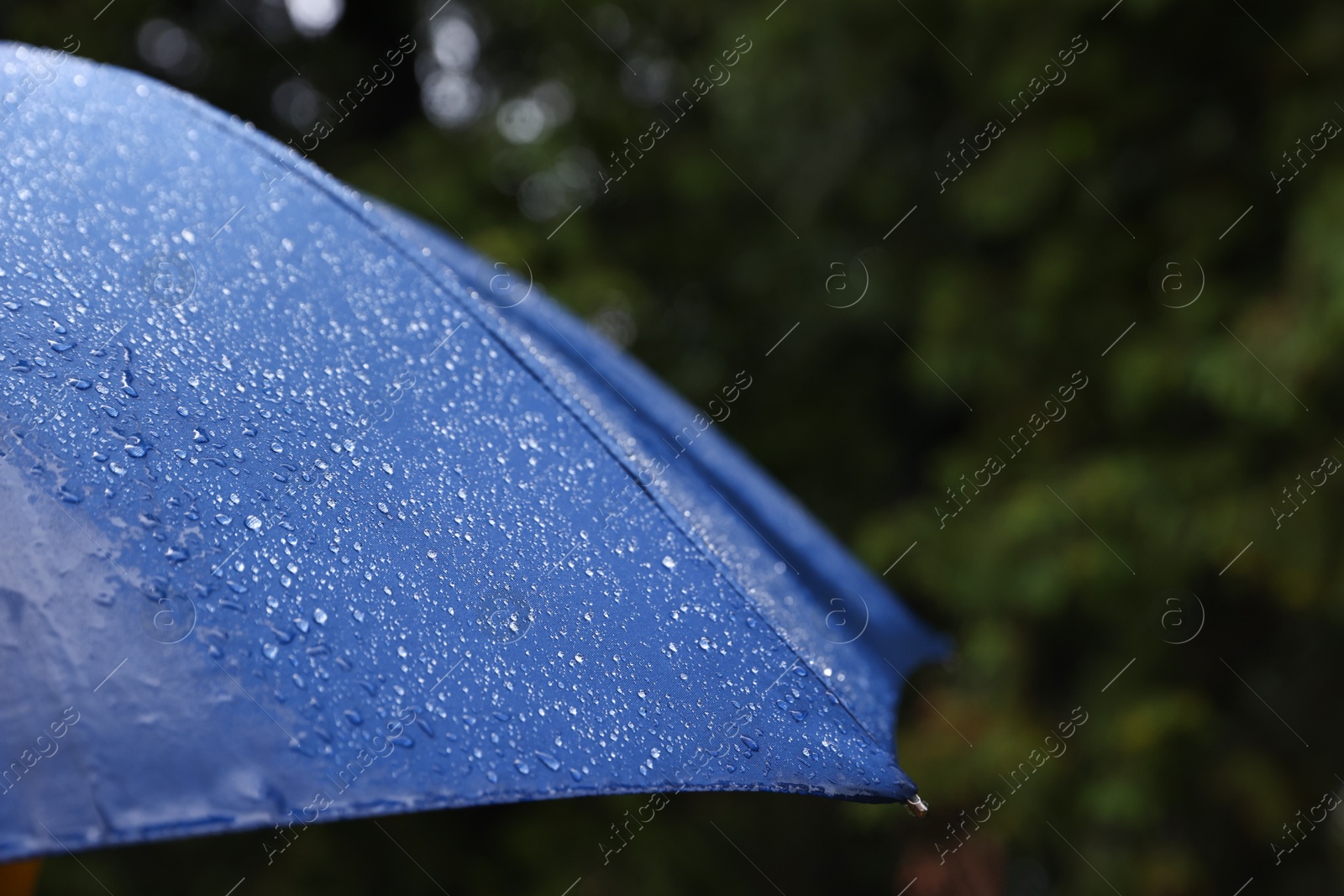 Photo of Blue umbrella under heavy rain outdoors, closeup. Space for text