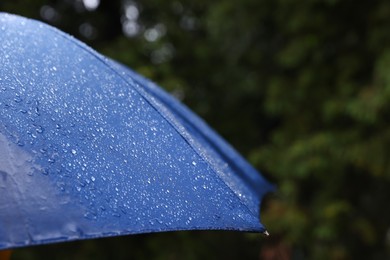Photo of Blue umbrella under heavy rain outdoors, closeup. Space for text