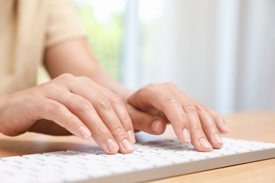 Photo of Woman typing on white wireless keyboard at wooden table, closeup