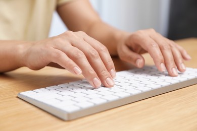 Photo of Woman typing on white wireless keyboard at wooden table, closeup