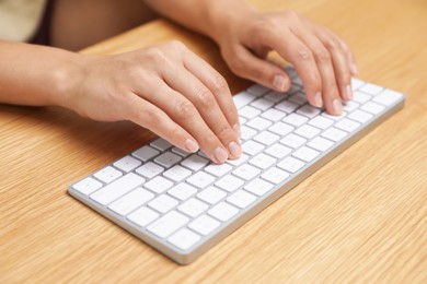 Photo of Woman typing on white wireless keyboard at wooden table, closeup