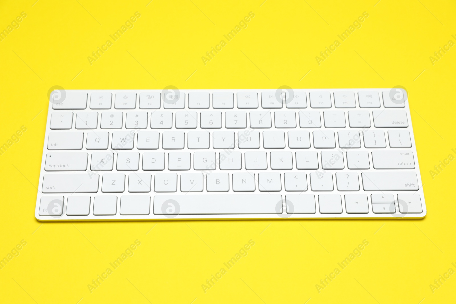 Photo of Modern white wireless keyboard on yellow background