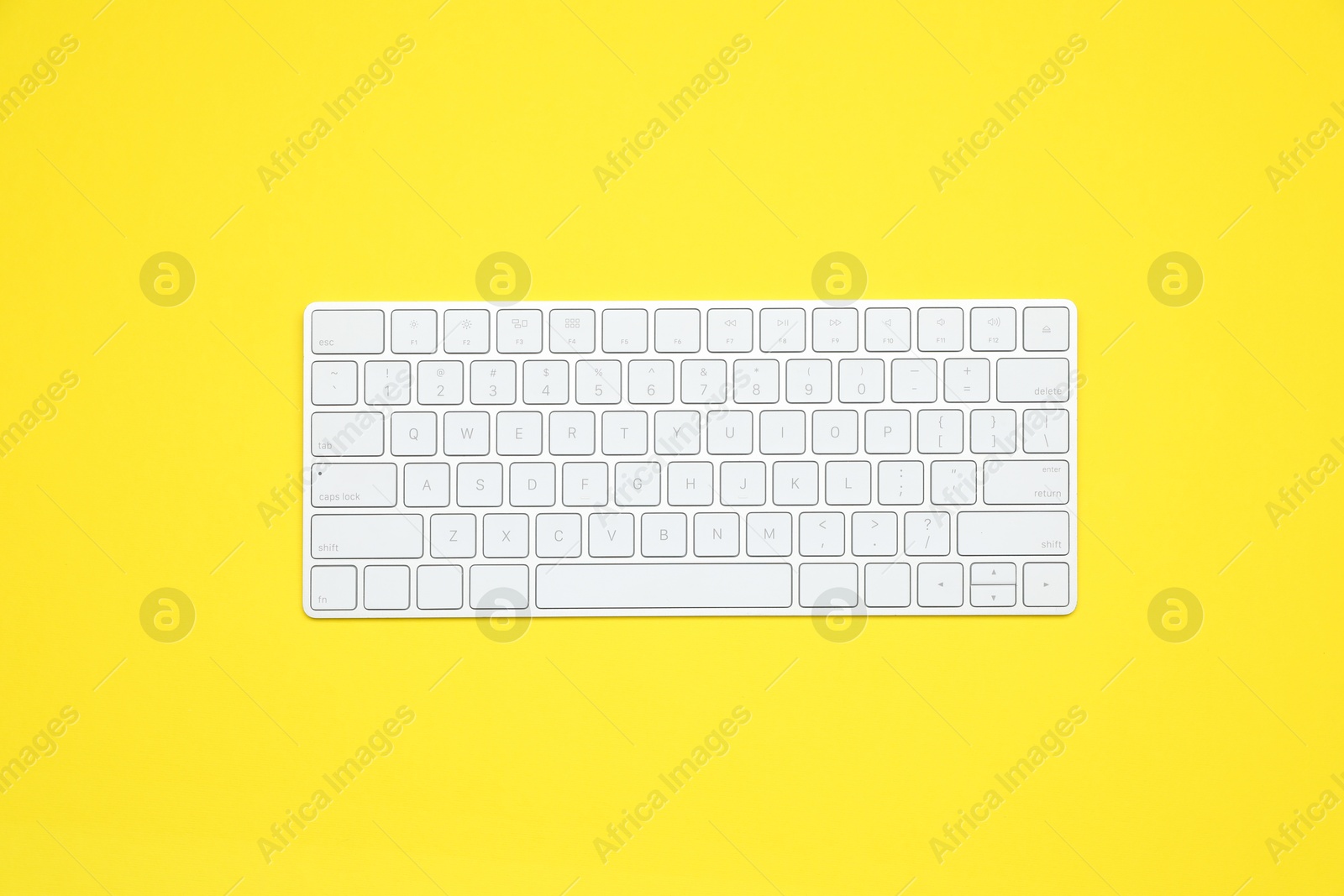 Photo of Modern white wireless keyboard on yellow background, top view