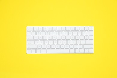 Photo of Modern white wireless keyboard on yellow background, top view