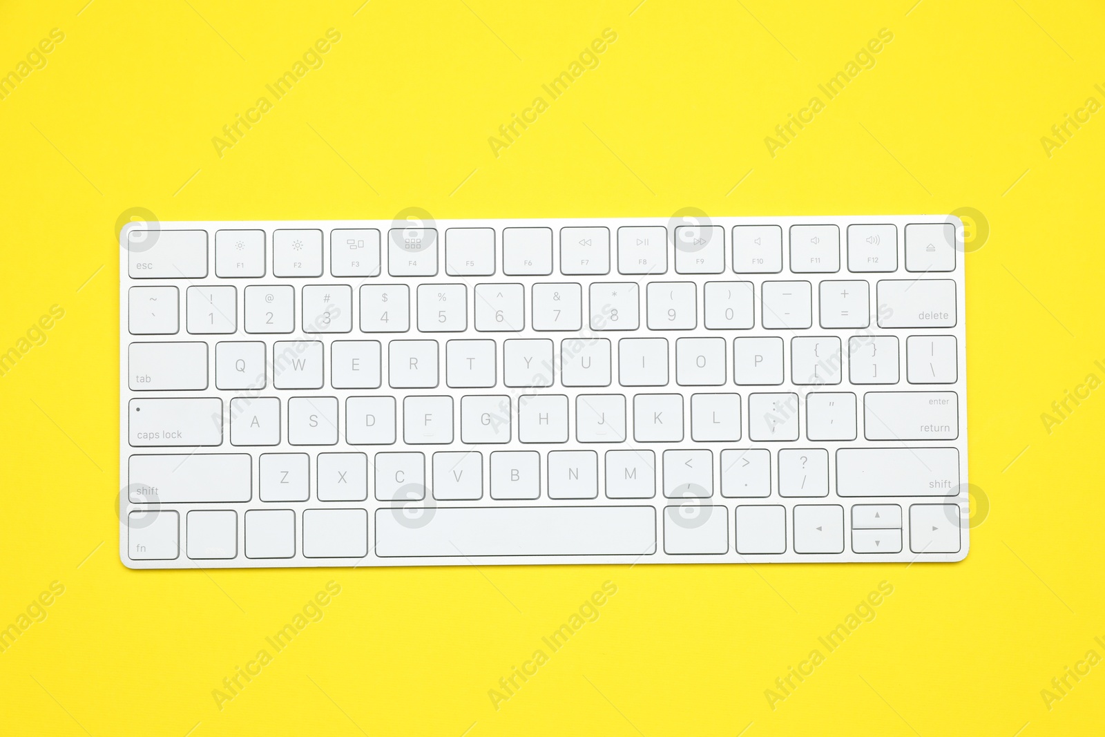 Photo of Modern white wireless keyboard on yellow background, top view