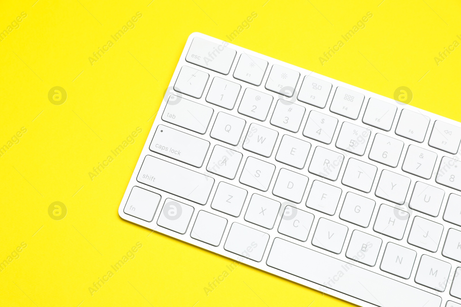 Photo of Modern white wireless keyboard on yellow background, top view. Space for text