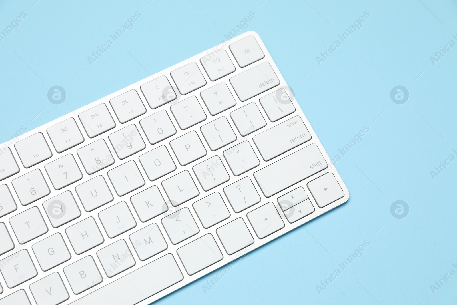 Photo of Modern white wireless keyboard on light blue background, above view