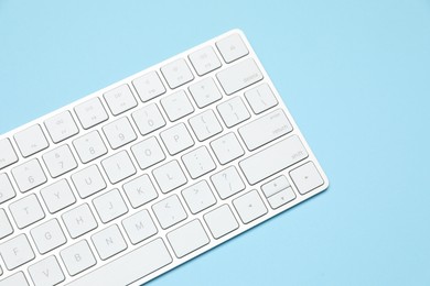 Photo of Modern white wireless keyboard on light blue background, above view