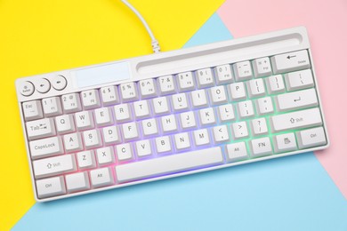 Photo of Modern white keyboard with RGB lighting on color background, top view
