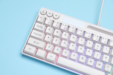 Photo of Modern white keyboard with RGB lighting on light blue background, above view