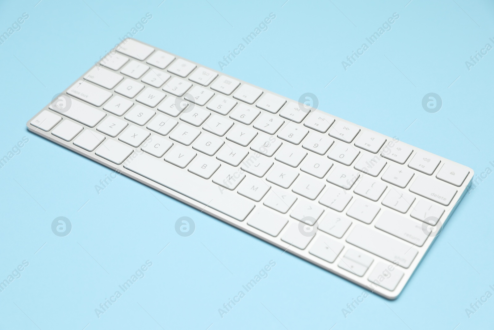 Photo of Modern white wireless keyboard on light blue background