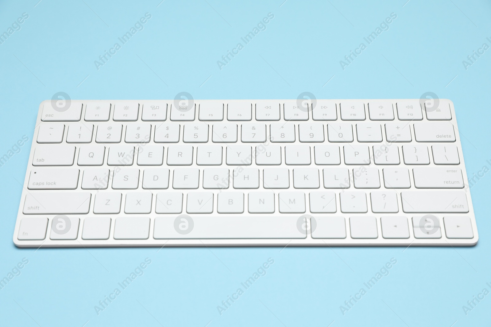 Photo of Modern white wireless keyboard on light blue background