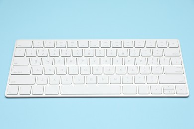 Photo of Modern white wireless keyboard on light blue background
