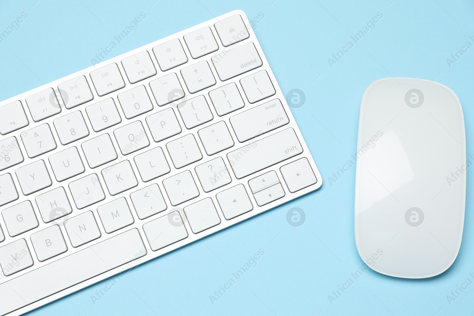 Photo of Modern white wireless keyboard and mouse on light blue background, top view