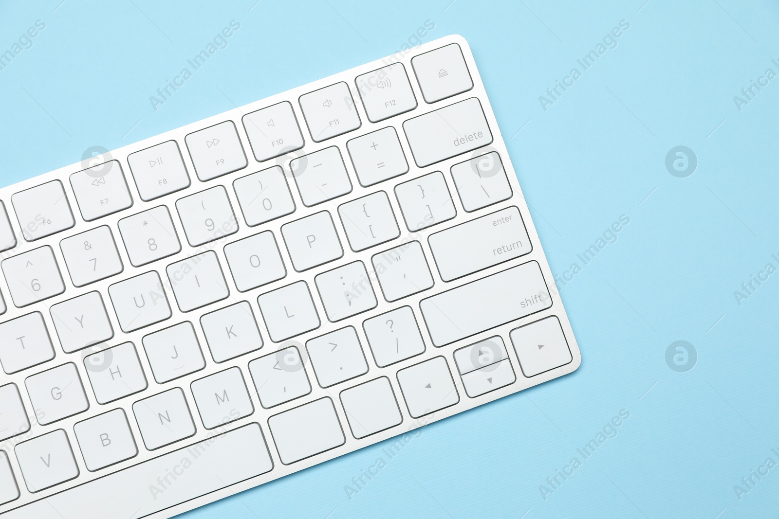Photo of Modern white wireless keyboard on light blue background, top view. Space for text