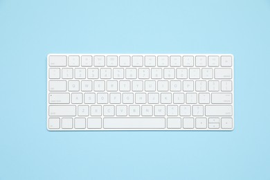 Photo of Modern white wireless keyboard on light blue background, top view