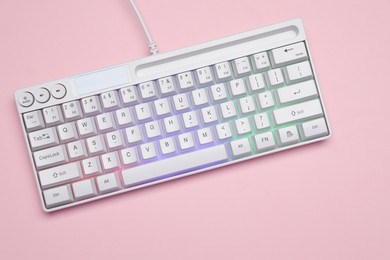 Photo of White keyboard with RGB lighting on pink background, top view. Space for text