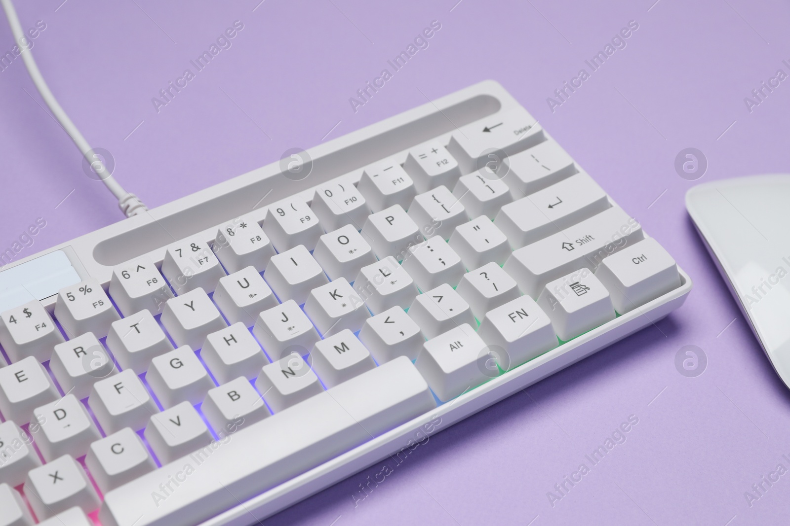 Photo of White keyboard with RGB lighting and mouse on violet background, closeup