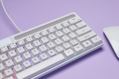Photo of White keyboard with RGB lighting and mouse on violet background, closeup