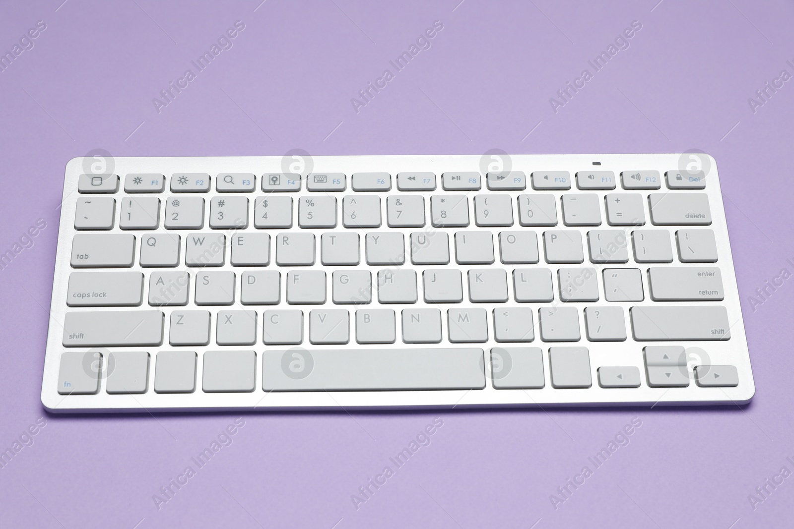 Photo of Modern white wireless keyboard on violet background