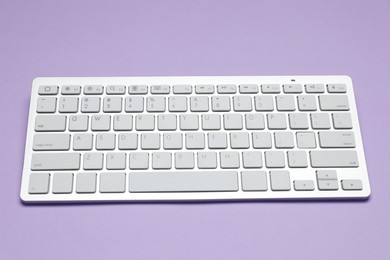 Photo of Modern white wireless keyboard on violet background