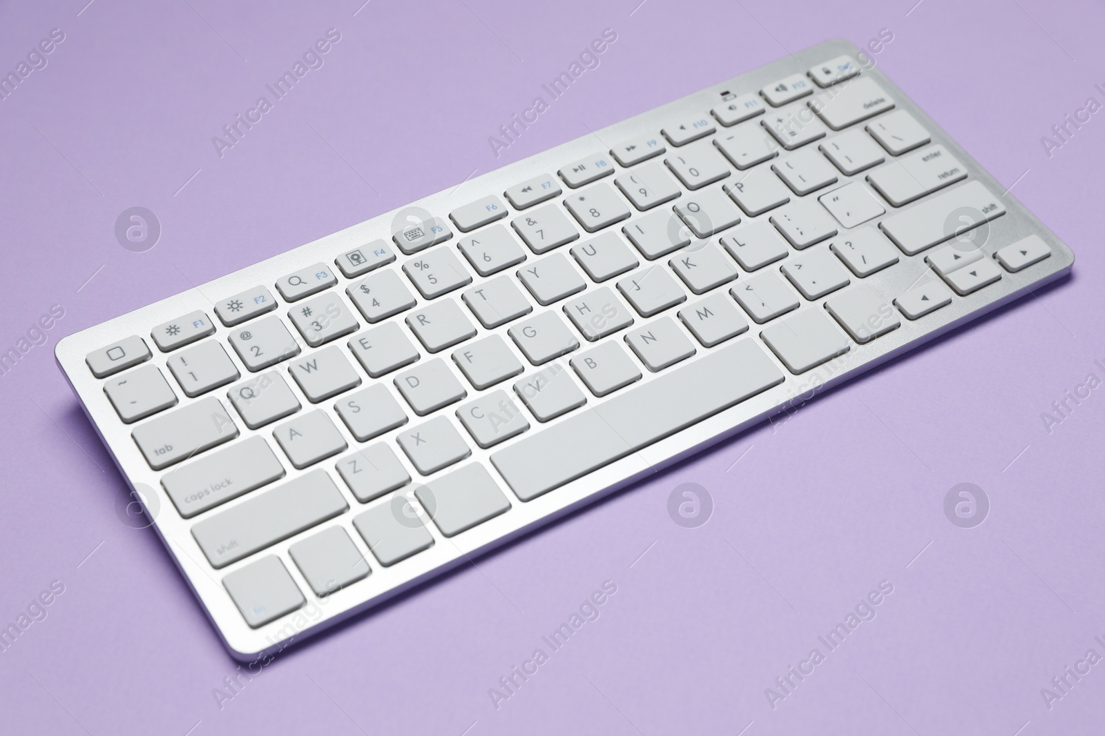 Photo of Modern white wireless keyboard on violet background