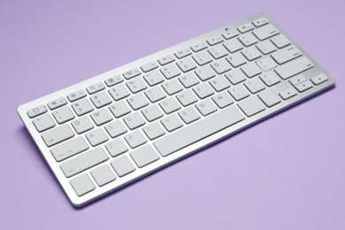 Photo of Modern white wireless keyboard on violet background