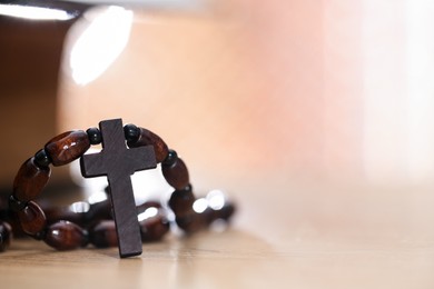 Photo of Rosary with wooden cross on table, closeup. Space for text