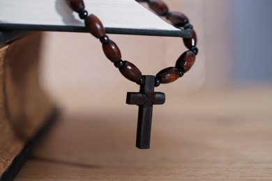 Photo of Rosary with wooden cross and Holy Bible on table, closeup