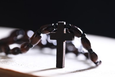 Photo of Rosary with wooden cross on Holy Bible against black background, closeup