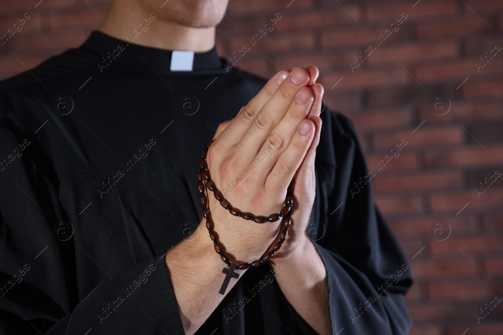 Photo of Priest with rosary praying near brick wall, closeup