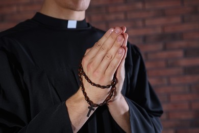 Photo of Priest with rosary praying near brick wall, closeup