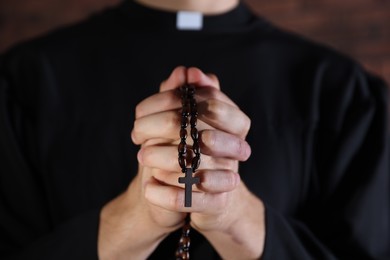 Photo of Priest with rosary praying on blurred background, closeup