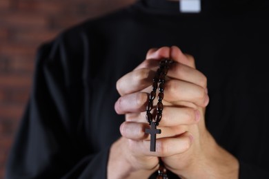 Photo of Priest with rosary praying on blurred background, closeup