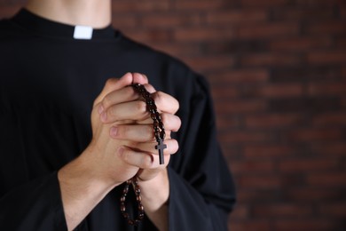 Photo of Priest with rosary praying near brick wall, closeup. Space for text