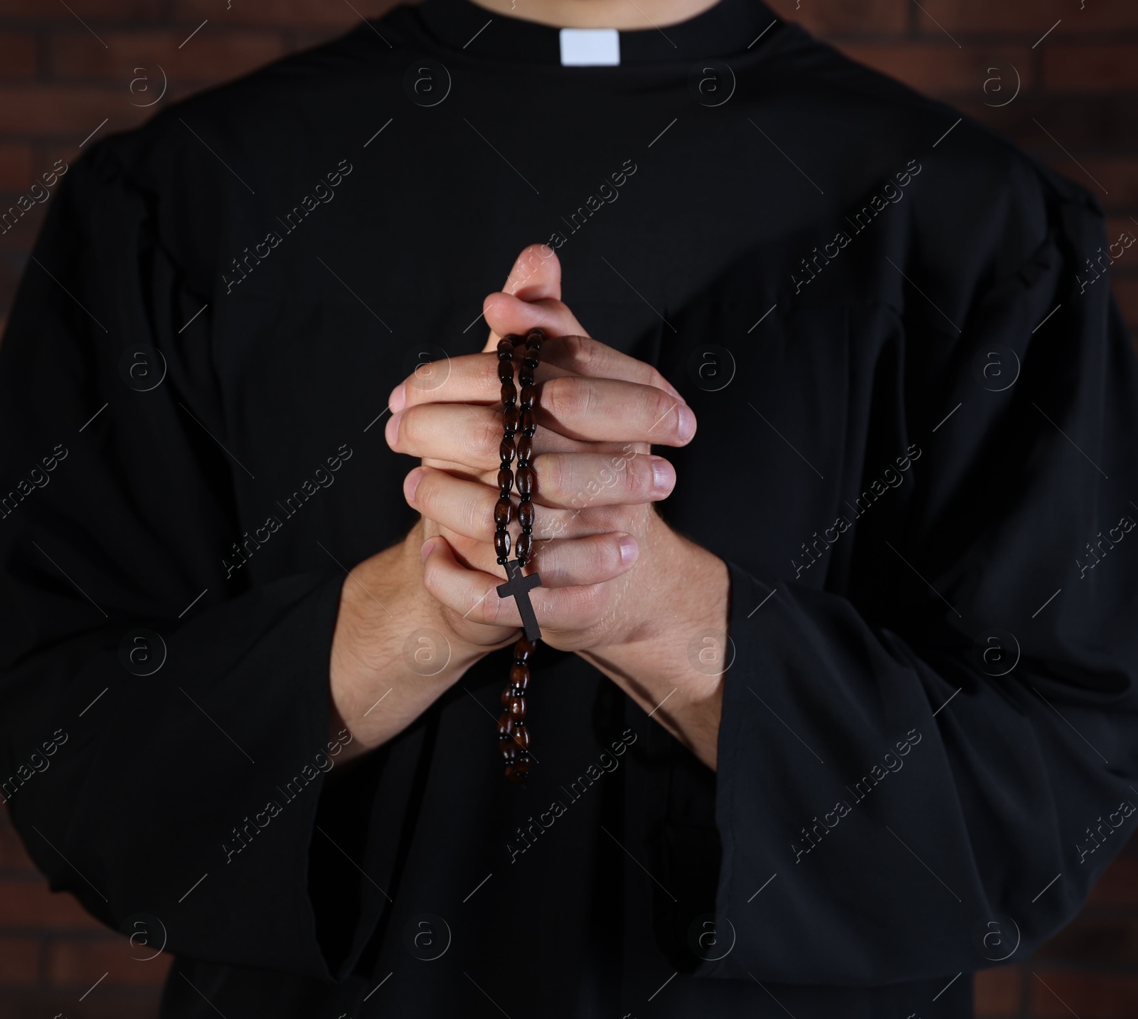 Photo of Priest with rosary praying near brick wall, closeup