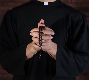 Photo of Priest with rosary praying near brick wall, closeup