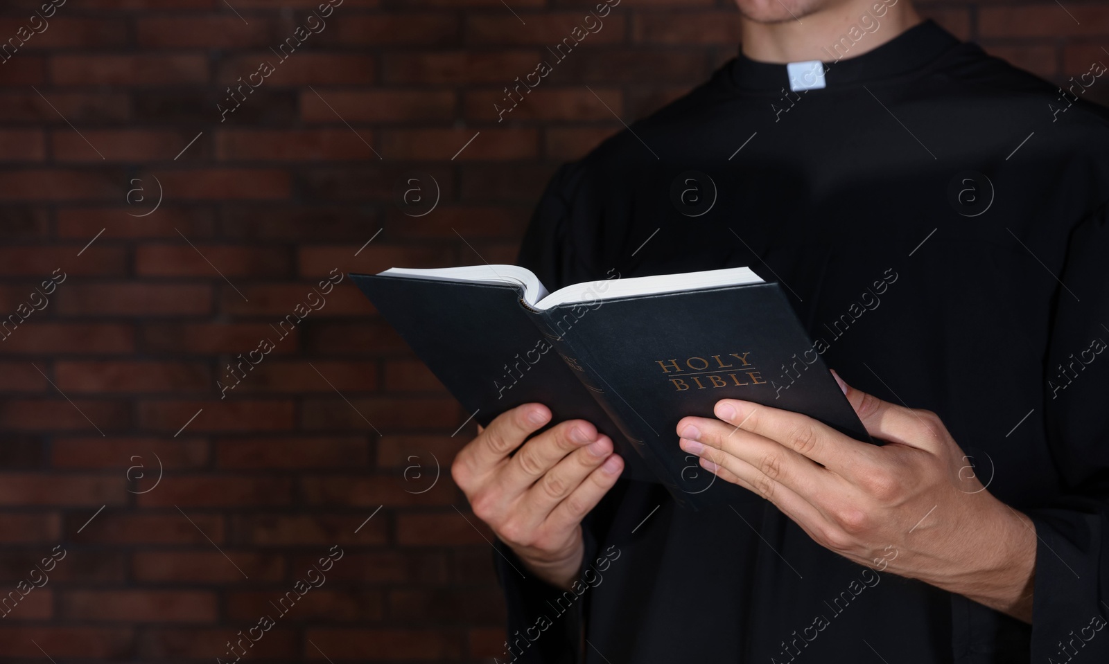 Photo of Priest with Holy Bible near brick wall, closeup. Space for text