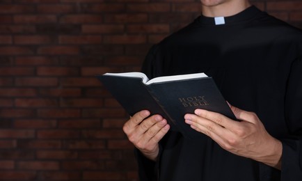 Photo of Priest with Holy Bible near brick wall, closeup. Space for text
