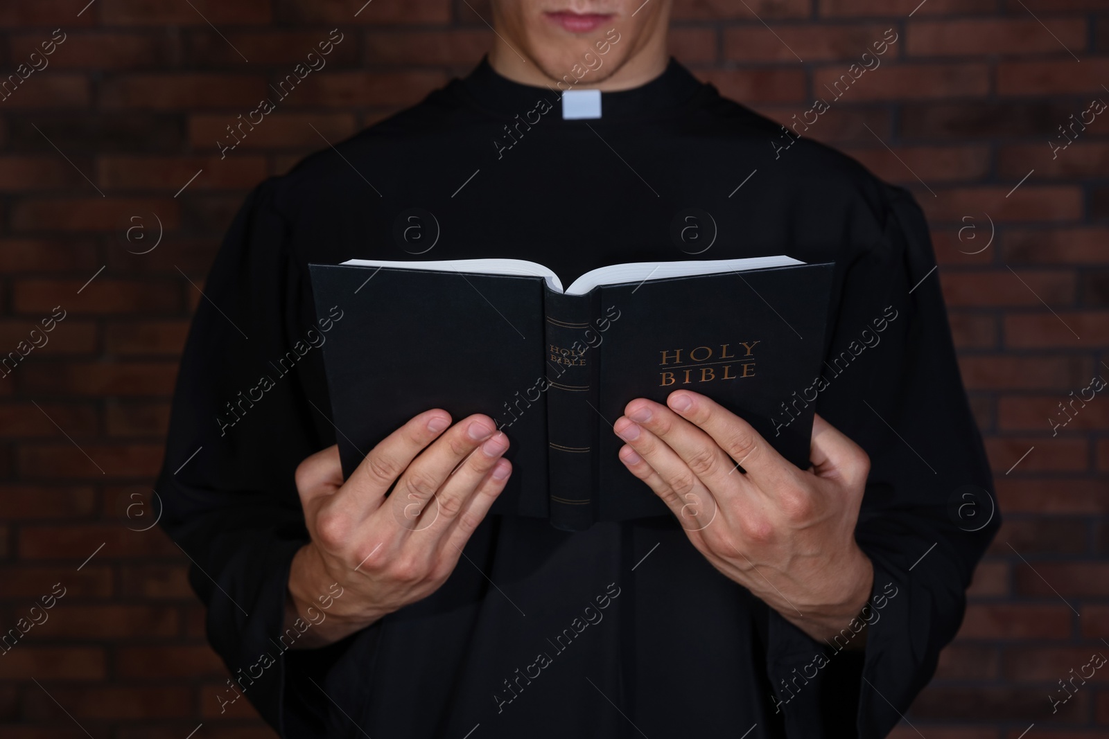 Photo of Priest with Holy Bible near brick wall, closeup