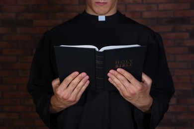 Photo of Priest with Holy Bible near brick wall, closeup