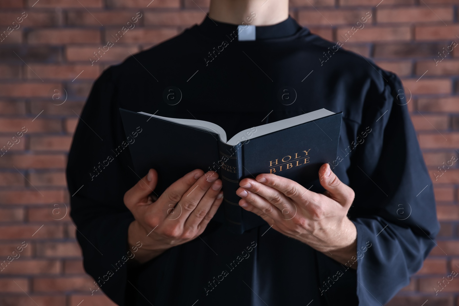 Photo of Priest with Holy Bible near brick wall, closeup