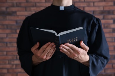 Photo of Priest with Holy Bible near brick wall, closeup