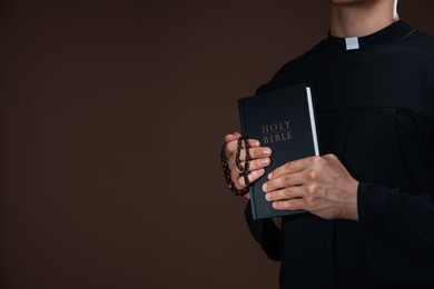 Photo of Priest with Holy Bible and rosary on brown background, closeup. Space for text