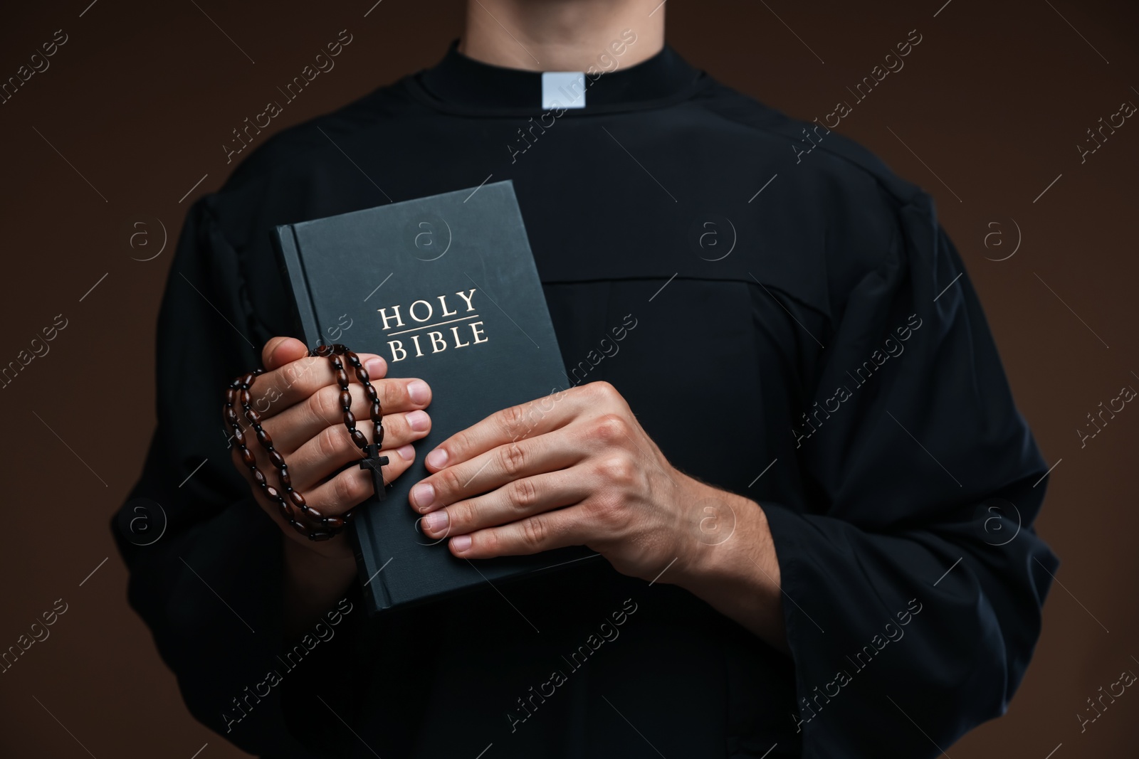 Photo of Priest with Holy Bible and rosary on brown background, closeup