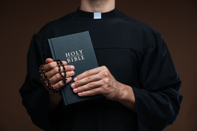 Photo of Priest with Holy Bible and rosary on brown background, closeup