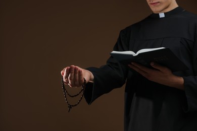 Photo of Priest with Holy Bible and rosary on brown background, closeup. Space for text