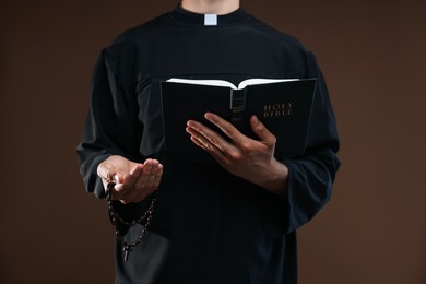 Photo of Priest with Holy Bible and rosary on brown background, closeup